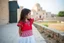 Placeholder: A five-year-old Palestinian girl wearing a traditional dress and new shoes looks to the side and points at a distant building.