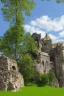 Placeholder: small gothic medieval house built into a rock face, rooms appear added on, lake, trees, arches, bridge, foliage, balconies, sunny blue sky