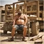 Placeholder: photography of a arab ugly burly serious wet sweaty, muscular chubby strong fat carpenter, shirtless, in broken dirty short pants, bulge, manly chest, very hairy, allover big goatee 46 years old, short hair, sitting with open legs on a little chair , on a construction site in the middle of a road, under the August sun, emotional eyes, , hyper-realistic, photorealistic , frontal view from the ground