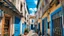 Placeholder: Narrow alleyway with beige and blue buildings, featuring clotheslines with white and colorful laundry hanging. The ground is paved with stones, and there are blue doors and windows on the buildings. The sky is clear with a few clouds