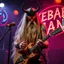 Placeholder: a very thin swedish viking man, evil with very long blonde hair (2 meter), (fat glowing eyes), he is called "KEBAB MAN" performing at death metal club, his name is "KEBAB MAN" kebab rolls On stage, kebab Neon lights and smog, and "KEBAB MAN" big sign on the wall, kebab tribal tattooes, spinning kebab machines, flames and smoke, chaos, he using gasolin and pour it on the guitar on the stage