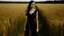 Placeholder: A young, dark-haired woman wearing a long black dress standing in a field of tall golden wheat