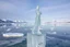 Placeholder: in a frozen sea with pretty mountains a full lady ice statue in artist pose standing over a ice block looking at camera, of clear glass like ice that going to melt and water drops fall from all body.