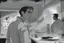 Placeholder: black and white storyboard, wide, on the Foreground there is a man in profile close to the camera and in the background, 3 chefs, scattered throughout the kitchen cooking, frying, cutting