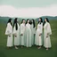 Placeholder: a group of women standing on top of a lush green hillside, inspired by Ren Hang, design milk, long black hair, whites, wanderers traveling from afar, trending on artisation, cloning spell, coat pleats, in twin peaks, submarine, by Helen Thomas Dranga, symetry, round-cropped, noire photo