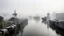 Placeholder: A foggy industrial landscape with ships docked along a river, surrounded by tall buildings in the background