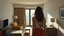 Placeholder: Habitación de hotel con mobiliario simple, una mujer de espaldas contemplando la ciudad desde la ventana, geometrías de luz sobre paredes desnudas, estilo óleo con estética cinematográfica