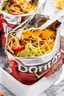 Placeholder: "Taco in a Bag" which consists of an open Doritos chip bag with sides rolled down, containing Doritos chips and cooked ground beef and lettuce and shredded cheese and chopped tomato pepper and onions and topped with more nacho chips, plastic fork, food blogger photography