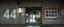 Placeholder: background of wall(wet textured concrete, gray, old, cracked, stained, 1 wall light) from underground parking, hong kong style, a large number "44" painted on left(old faded paint), at middle is an opening into an area with asian shops, cyberpunk, to the right of opening a faded painted rectangle containing alien language for obey