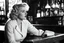 Placeholder: a profile view of Norma Jeane, a.k.a. the young Marilyn Monroe, She is sitting at a bar, elegant and sad, on a high stool. It is noon, and the light is streaming in, she is sad