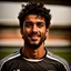 Placeholder: 85mm DSLR color photography of a very detailed headshot fitting all of head and hair in frame. 23-year-old English soccer player, with black hair color and with facial hair and has a brown light skin tone with a small smile, grey background