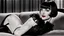 Placeholder: louise brooks, dressed in stockings and stilettos, with a black bob hairstyle with bangs and dark sultry eyes and red lips, lying on a couch, smiling.