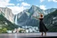 Placeholder: A modern city at the foot of the mountain. The entrance valley with a waterfall from a high rock. A beautiful lady dancer showing her performance in a poen stage in a top and midi skirt.