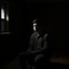 Placeholder: A young man sitting in a room that is half dark and half lit