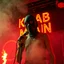 Placeholder: a very thin swedish man, with a skimask with only a hole for the mouth (no eyes), he is called "KEBAB MAN" performing at death metal club, his name is "KEBAB MAN" kebab rolls On stage, kebab Neon lights and smog, and "KEBAB MAN" big sign on the wall, spinning kebab machines, flames and smoke, chaos, he singing with mic,
