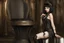 Placeholder: a skinny Cleopatra, with a bob hairstyle, in black boots, standing next to a black gothic seat, in a steampunk setting.