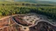 Placeholder: Climate emergency. Aerial view of a deforested area, with only a few scattered tree stumps remaining amidst the barren, exposed soil. Heavy machinery stands idle, and the surrounding forest appears dense and untouched, contrasting sharply with the cleared land. Beautiful award-winning photograph, shocking, rule of thirds, balanced delightful composition, perfect lighting, superb detail, 16k render