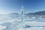 Placeholder: in a frozen sea with pretty mountains a full model lady statue made of frozon water in artist pose standing over frozon water looking at camera, of clear glass like ice that going to melt and water drops fall from all body.