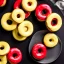 Placeholder: Yellow and red and black donuts on a plate on a black table