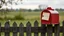 Placeholder: an old wooden fence with a little bird on it, a red old mailbox on the fence, a big note stuck on the mailbox