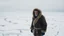 Placeholder: A desolate winter landscape with snow cutting the earth into fragments, a lone Inuit man in traditional fur clothing trudging through the blizzard, his face weathered and stoic, under a heavy, gray sky.