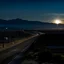 Placeholder: night time, a lonely highway, leading to a beautiful city in the distance. Behind the city is a mountain range with the sun rising