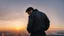 Placeholder: An Englishman in a bomber jacket standing to one side of a tall building looking across a city at sunset