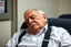 Placeholder: Cree l image d un agent de sécurité proche de la retraite. Il porte des bretelles. Il a une chemise blanche. Il a une petite moustache. Il dort sur une chaise.