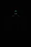 Placeholder: Inside a dark, shadow-filled computer screen, a sinister humanoid silhouette emerges. The silhouette has a tall, gaunt figure with elongated limbs and a bald head. Its hollow black eyes glow faintly, directly fixating on the viewer, creating an intense and unnerving connection. The monstrous figure is centrally positioned within the screen, enhancing the sense of dread and malevolent presence emanating from within the digital realm. The surrounding room remains dark and oppressive, with minimal