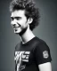 Placeholder: A slim relatively high guy with wild curly light hair, smiling with teeth and wearing black skinny jeans and a t-shirt