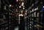 Placeholder: full-height shot of a woman in a tight black dress, inside a large magic book shop, shelving, lights, books, bottles, windows