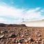 Placeholder: Fotografia di un paesaggio con un terreno roccioso o arido in primo piano e un cielo azzurro con nuvole bianche sullo sfondo e un grosso muro di cemento con cantiere. L'immagine è molto nitida.