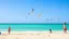 Placeholder: A bright summer day at the beach, with clear blue skies, children playing in the sand, and a flock of gulls soaring above, set against the dazzling turquoise sea.