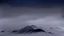 Placeholder: misty foreground and night sky, no sun, single narrow mountain peak coming through the mist