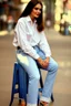 Placeholder: Pretty woman sitting on a stool, wears hunge open white shirt and blue jeans