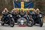 Placeholder: a very hard and tuff motorcycle young gang with long blond Sweden viking hair, not old, posing with their Harley Davidsson bikes, some of them holding guns and shotguns, a logo sign with Falköpings HD Club, "Fearless sinners" Skulls and bones, skeletons and fire, Sweden vikings DEMONS, Swedish flag
