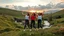 Placeholder: a group of young ladies in sports pants and blouse are dancing to camera in high grassy hills,a small fall and river and wild flowers at river sides, village houses,some trees ,cloudy sun set sky