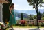 Placeholder: very beautiful lady with beautiful midi green- silver,jeweled lace skirt and pretty same material top with curvy hair high heels standing in a nice villa yard with trees flowers ,in country side in floor of beautiful mountains ,sea with ships ,water falls,16 by 9