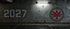 Placeholder: background of firing squad execution wall(wet textured concrete, gray, old, cracked, billet holes, blood stained, 1 wall light) from underground parking, german style, a large blocky upside down "2027" painted on left(old faded paint, red stains running down and past), cyberpunk, mural on right of Republic of Gilead logo
