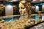 Placeholder: pool mosaic, 3D mirror pieces, beautiful composition, holographic marble pieces, brunette female, dessert shop, flowers, ethereal in sunshine, shading pastel and charcoal golden and ochre, golden glitter, , golden patina, corrosion