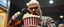 Placeholder: pop corn bucket that looks like a chain saw wielded by serious angry bald law man, in cinema