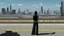 Placeholder: Tall thin woman, with straight black hair, dressed in a camouflaged jumpsuit, looking out from the rear of a futuristic aircar, on a tarmac runway, with a city skyline in the distance