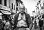 Placeholder: man looking like "Walter White" in breaking bad tv show, bald and goatee glasses, with bare chest riding on a camel in a alley Casablanca town, panorama, black and white photo, lot of markets and people in background, camera in the back of him