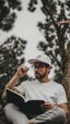 Placeholder: A man wears a white Dad Hat and wears glasses and is busy reading with a tree behind him, high resolution, and the image focuses on the Dad Hat