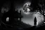 Placeholder: scene, horizontal black and white, forest fog, superbig full moon, moon is a center of image, tim burton character, woman wiht cape and hood, woman stand up on spiral rock, face woman sad, super big eyes, circles eyes, background old house, high house more rooms, backlight, sad,