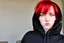 Placeholder: A woman with short, bright red hair, brown eyes, wearing a black hoodie.