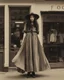 Placeholder: full-length, young woman dressed like a modern-day witch, floaty clothing, with dark hair, outside a shop