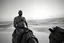 Placeholder: man looking like Walter White in breaking bad, bald, with bare chest riding on a camel in sahara in desert, panorama, black and white photo, staring at horizon