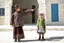 Placeholder: A five-year-old Palestinian girl wearing a traditional dress and new shoes looks to the side and points at a distant building.