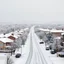 Placeholder: a glimpse of the suburban city, everything is covered in snow, the landscape seems to be made of felt, pastel colours, some people and cars